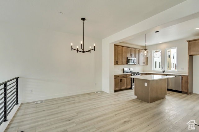 Kitchen with stainless steel appliances, an inviting chandelier, light hardwood / wood-style flooring, a center island, and hanging light fixtures