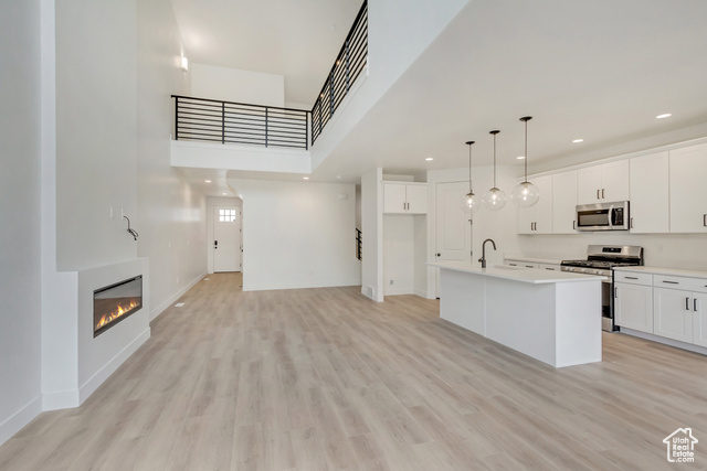 Kitchen featuring a center island with sink, white cabinets, hanging light fixtures, and appliances with stainless steel finishes