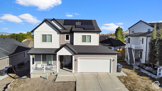 View of front of home with covered porch, a garage, and solar panels