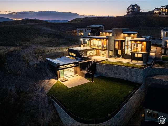 Back house at dusk featuring a lawn, a patio area, and a mountain view