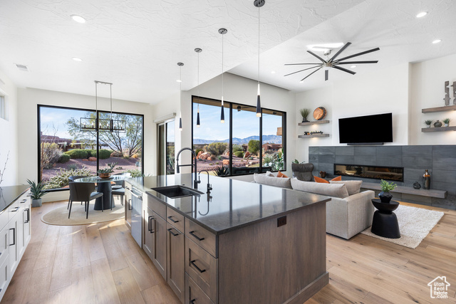 Kitchen with sink, a tile fireplace, decorative light fixtures, white cabinetry, and an island with sink