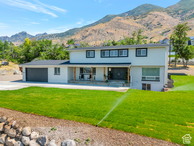 View of front of house with covered porch, a mountain view, a garage, and a front lawn