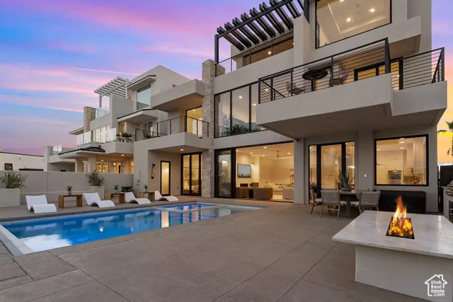 Back house at dusk featuring a fenced in pool, a patio, and an outdoor fire pit