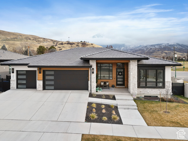 Modern home with a mountain view, a garage, a front lawn, and covered porch