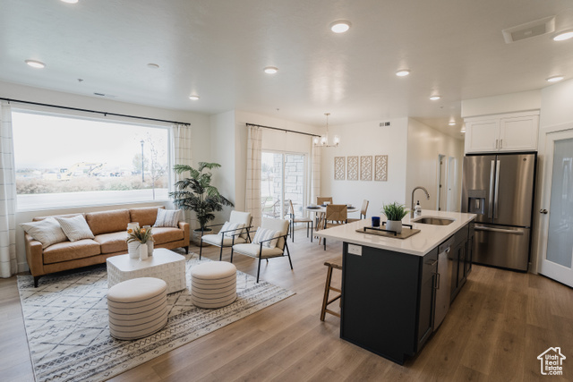 Kitchen featuring appliances with stainless steel finishes, sink, a center island with sink, decorative light fixtures, and white cabinets