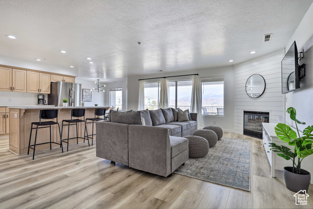 Living room with a fireplace, light wood-type flooring, a textured ceiling, and an inviting chandelier