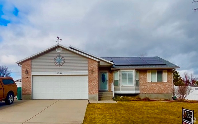 Single story home with solar panels, a garage, and a front lawn