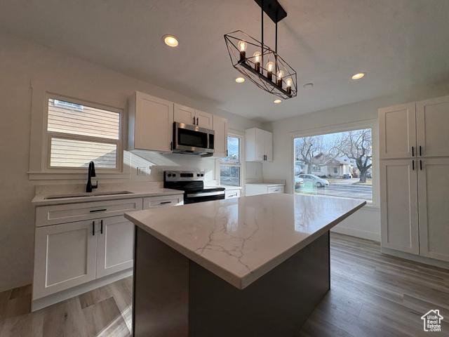 Kitchen with stainless steel appliances, sink, decorative light fixtures, a center island, and white cabinetry