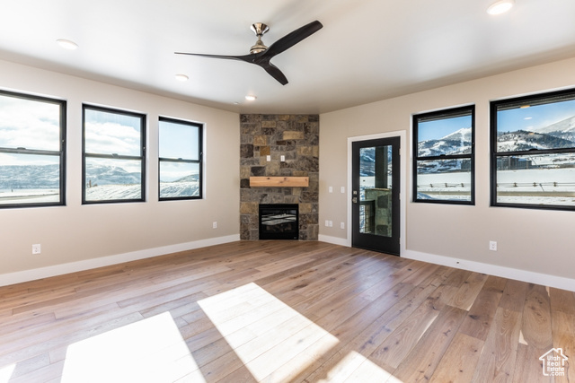 Unfurnished living room featuring a stone fireplace, ceiling fan, and light wood-type flooring