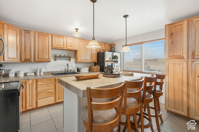 Kitchen with black range with electric stovetop, a breakfast bar, sink, light tile patterned floors, and a kitchen island