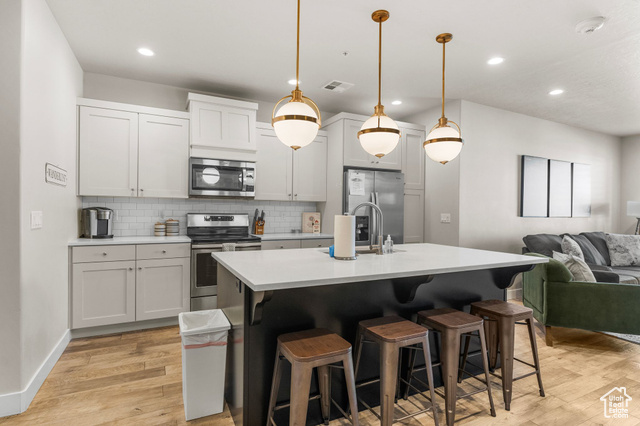 Kitchen featuring hanging light fixtures, backsplash, a breakfast bar area, a center island with sink, and appliances with stainless steel finishes