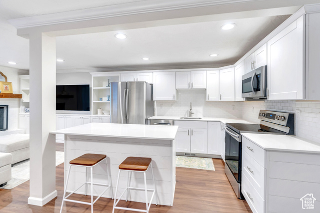 Kitchen with stainless steel appliances, a kitchen bar, light wood-type flooring, white cabinetry, and sink