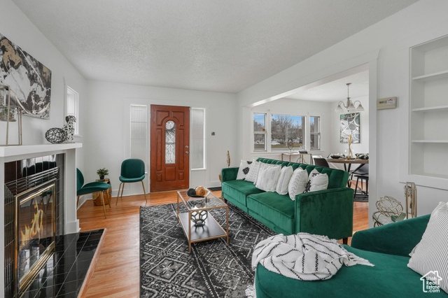 Living room featuring a textured ceiling, a tile fireplace, a notable chandelier, hardwood / wood-style floors, and built in features