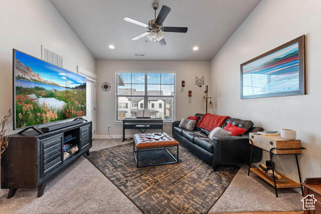 Carpeted living room featuring ceiling fan and vaulted ceiling