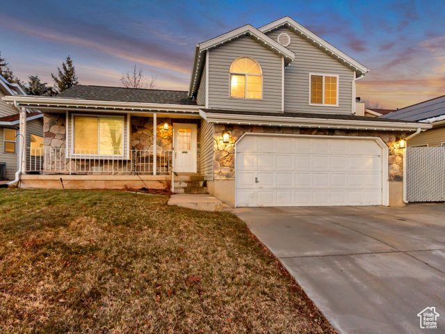 Front facade featuring a garage, a porch, a yard, and central AC unit