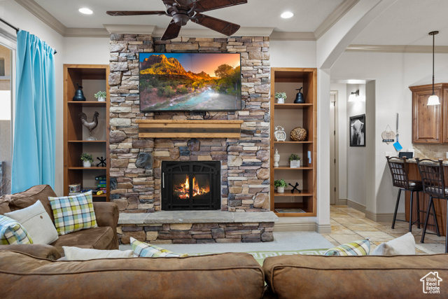 Living room featuring ceiling fan, built in features, crown molding, and a fireplace