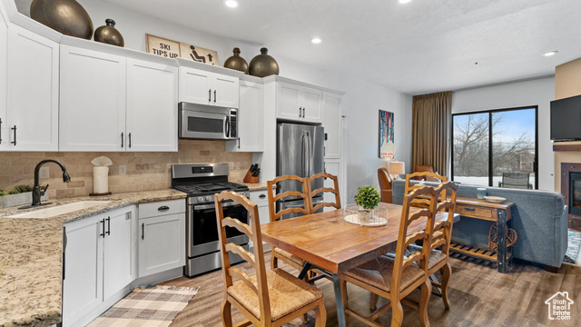 Kitchen featuring white cabinets, stainless steel appliances, light stone countertops, and sink