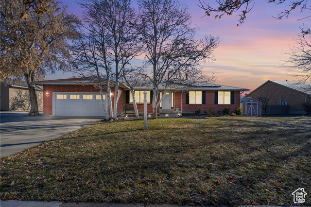 Ranch-style home with a garage, a storage unit, and a lawn