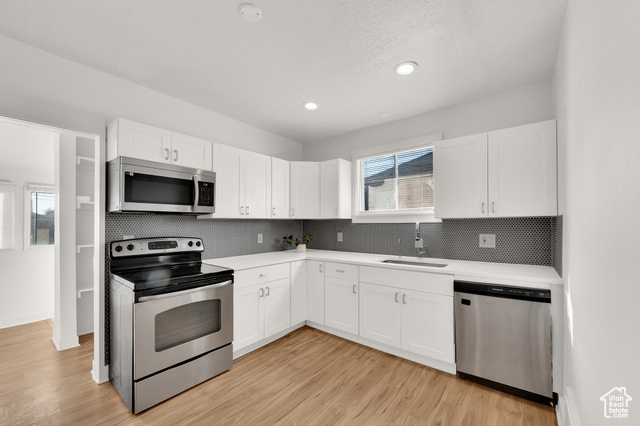 Kitchen with sink, white cabinetry, stainless steel appliances, tasteful backsplash, and light hardwood / wood-style floors