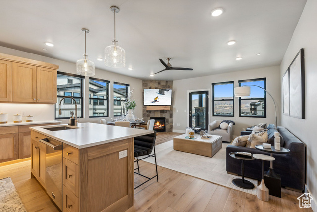 Kitchen featuring sink, hanging light fixtures, light wood-type flooring, an island with sink, and a fireplace