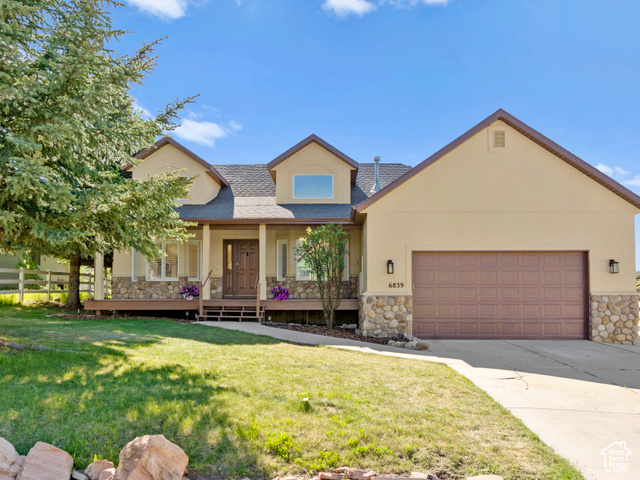 View of front of property featuring a garage, covered porch, and a front lawn