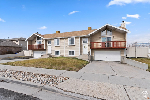 Split foyer home featuring a garage, a front yard, concrete driveway, and fence